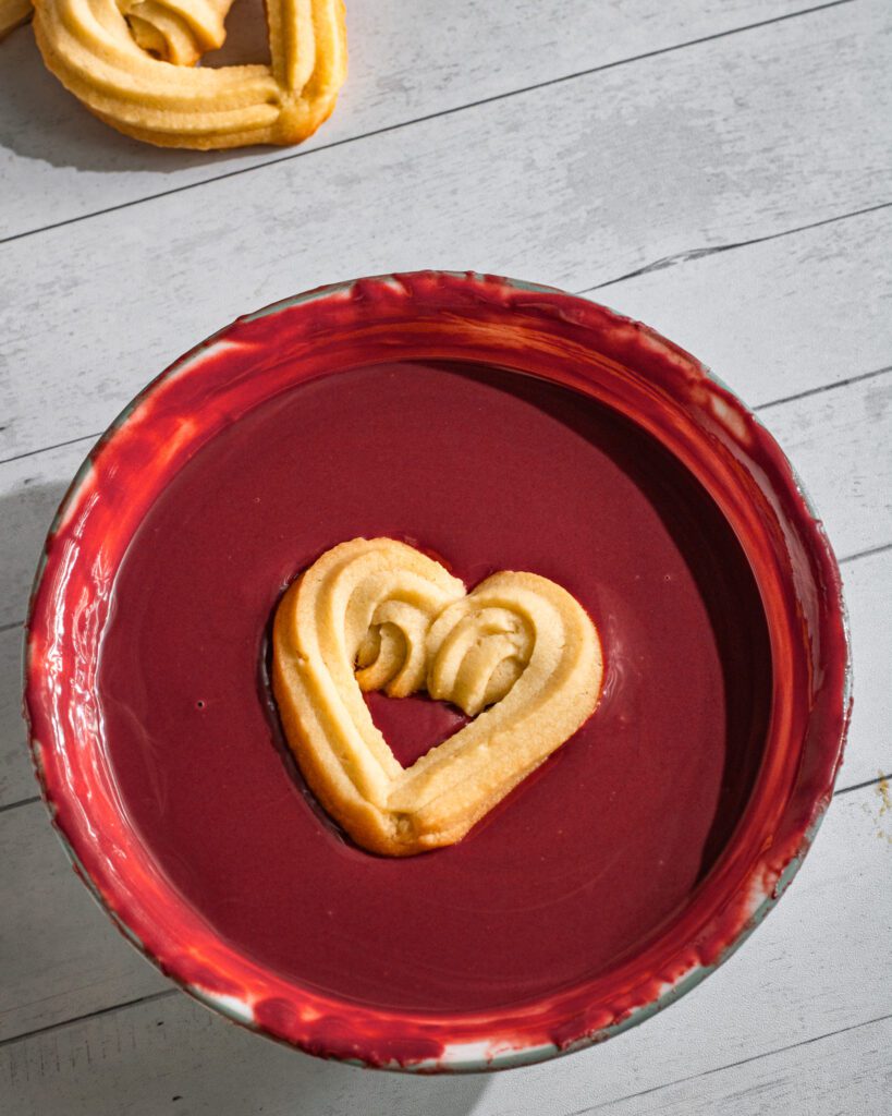 Hand-piping eggless butter cookie dough into heart shapes in red chocolate