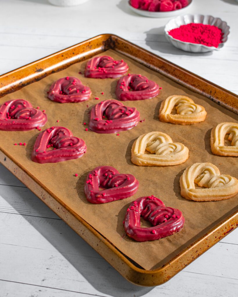 Eggless chocolate-dipped heart cookies stacked on a tray