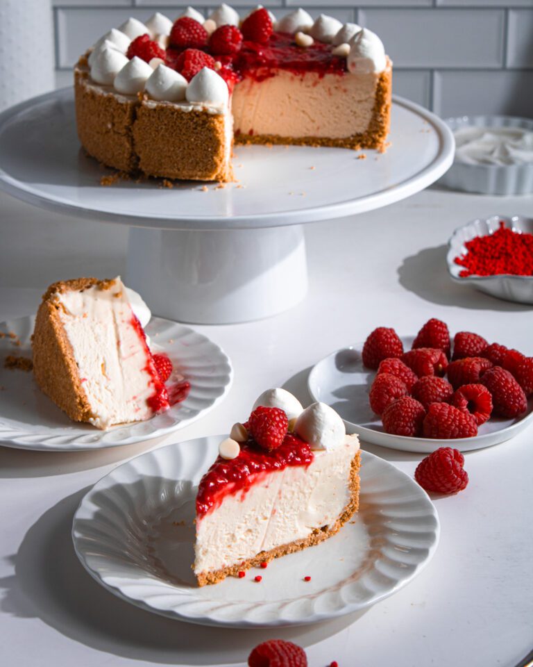 Slice of no-bake white chocolate raspberry cheesecake on white plate