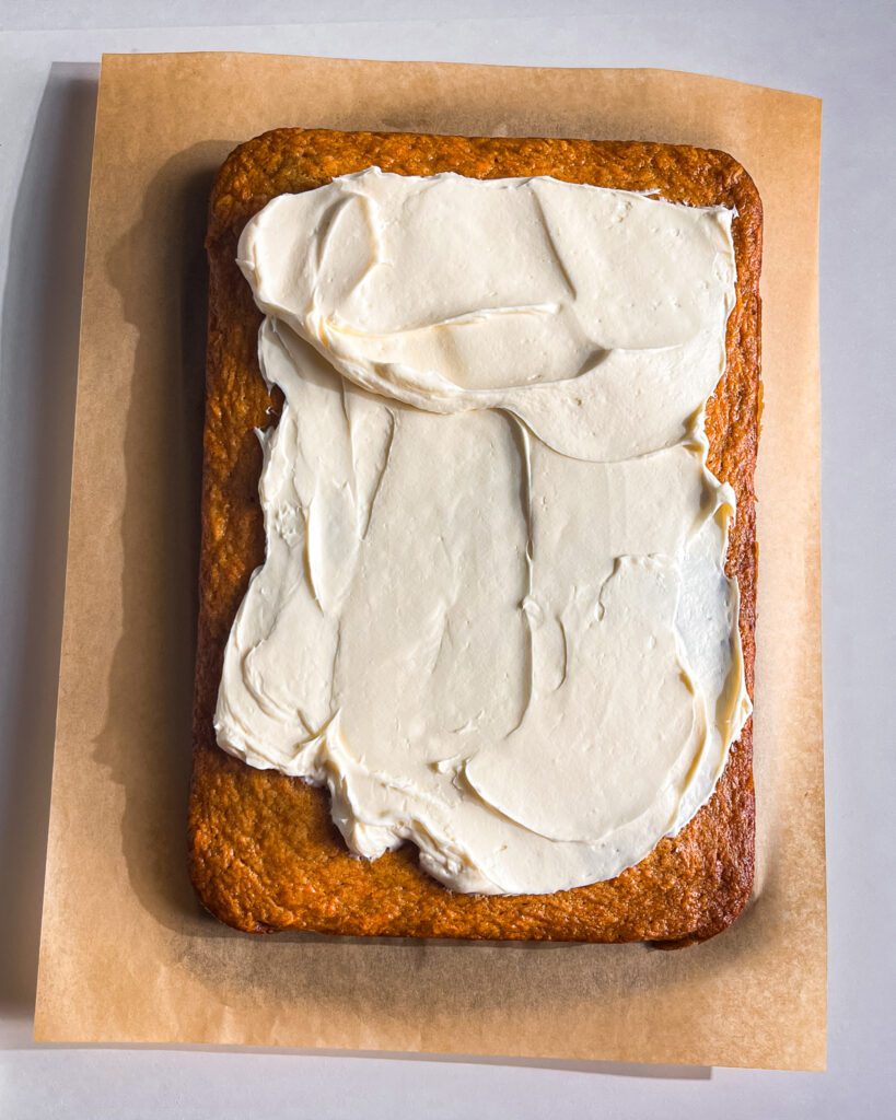 spreading cream cheese frosting over eggless carrot cake